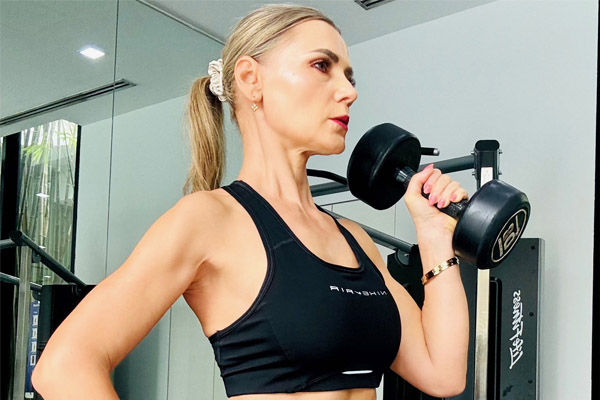 Essential Package - Nicoleta Binggeli, founder of SheTrains, performing a bicep curl in a gym. She is wearing a black sports bra and leggings, showcasing her toned physique. Discover our programs